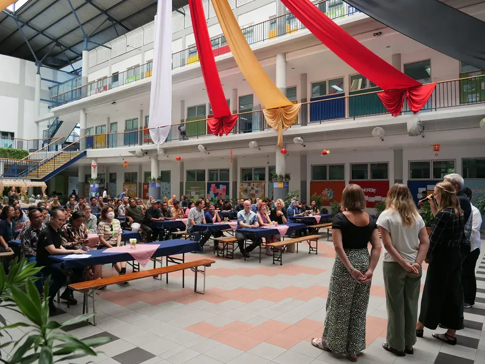 A group of people are standing in a courtyard with tables and benches.