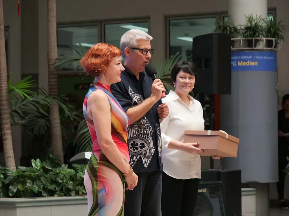 A man speaking into a microphone while a woman holds a box