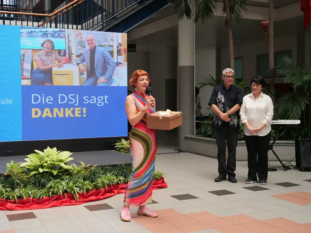 A woman stands in front of a sign that says die dsj sagt danke