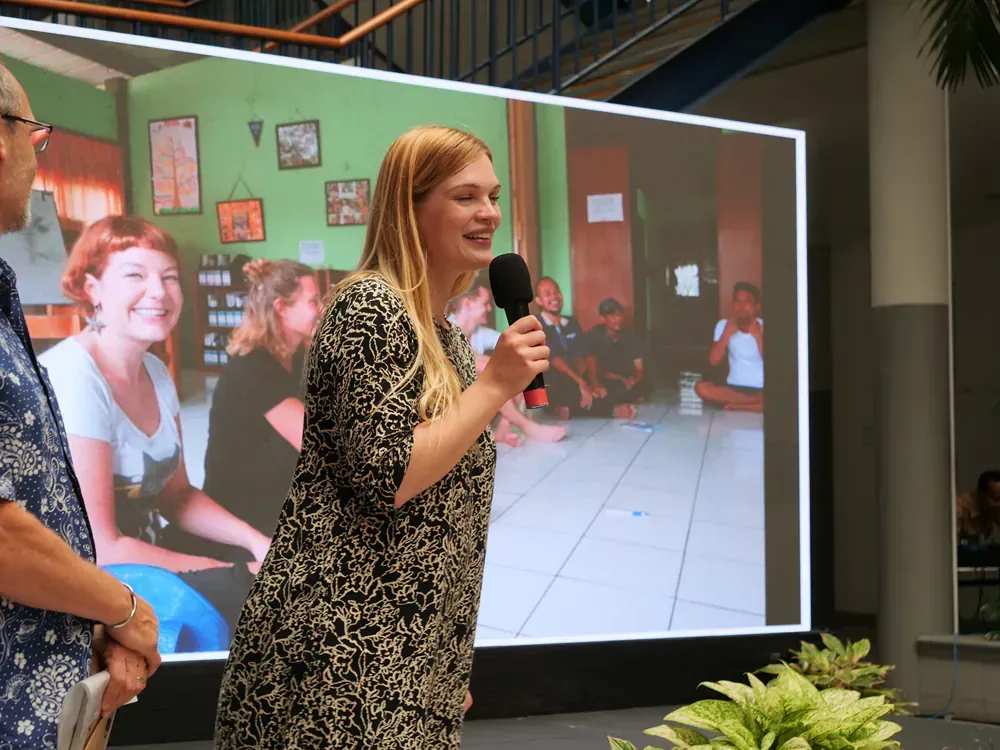 A woman speaking into a microphone in front of a large screen