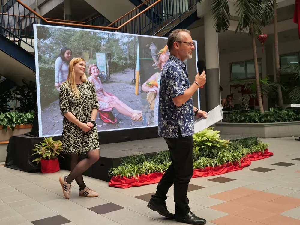 A man and a woman are standing in front of a large screen.