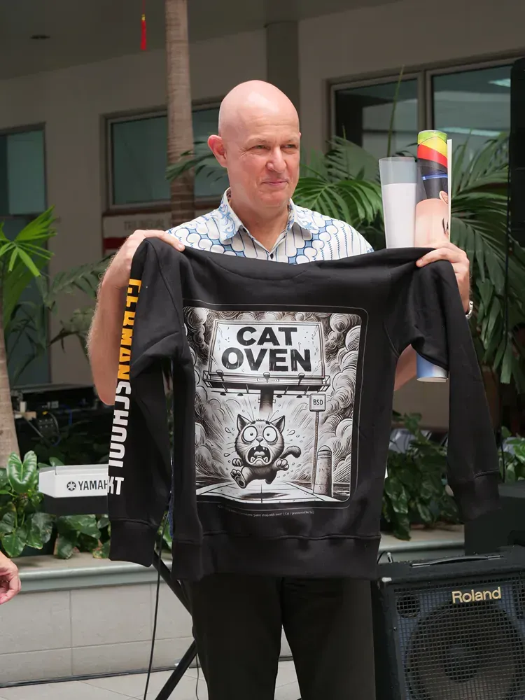 A bald man is holding a black shirt that says cat oven