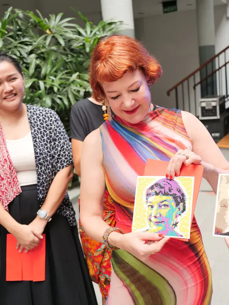 A woman in a colorful dress is holding a painting of a woman 's face.