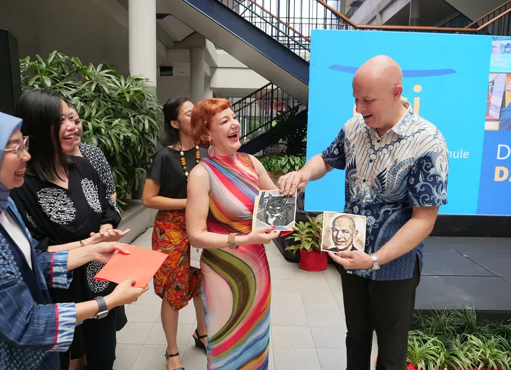 A group of people are standing around a man giving a woman a cd.