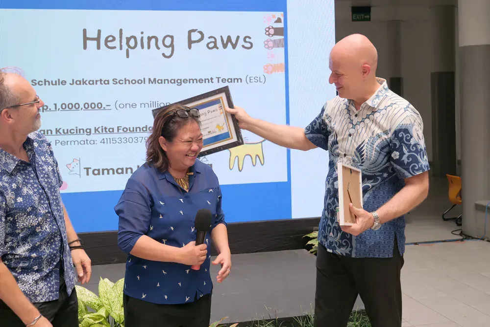 A man is giving a woman a certificate in front of a screen that says helping paws.