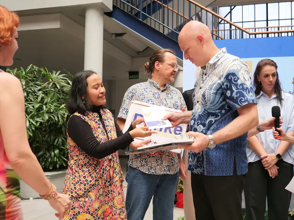 A man in a blue shirt is giving a woman a book