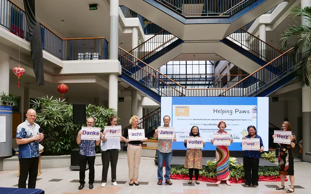 A group of people are holding signs in front of a large screen in a building.