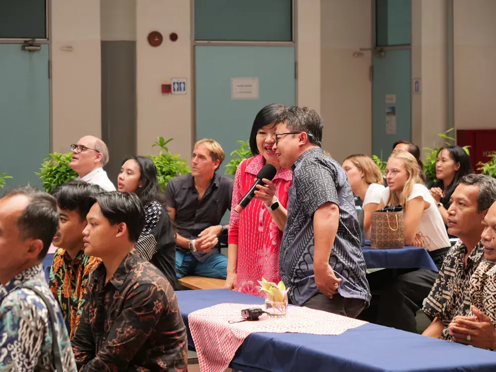 A group of people are sitting at tables in a room with a woman holding a microphone.