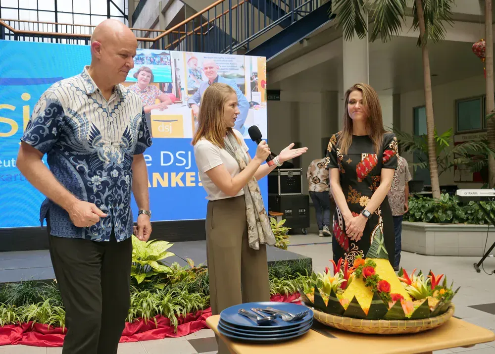 A man and two women are standing next to a table with plates and flowers on it.