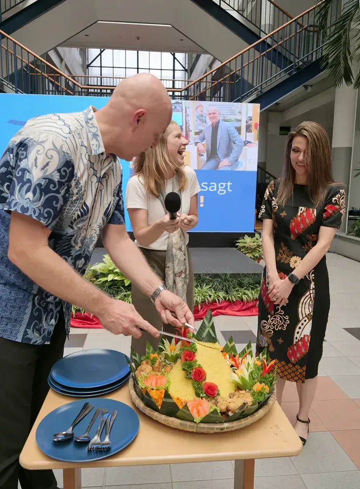 A man in a blue shirt is cutting a cake