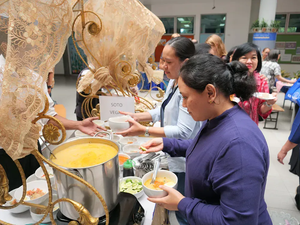 A group of people are standing around a table eating soup.