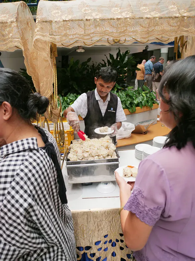 A man in a vest is serving food to a woman in a purple shirt
