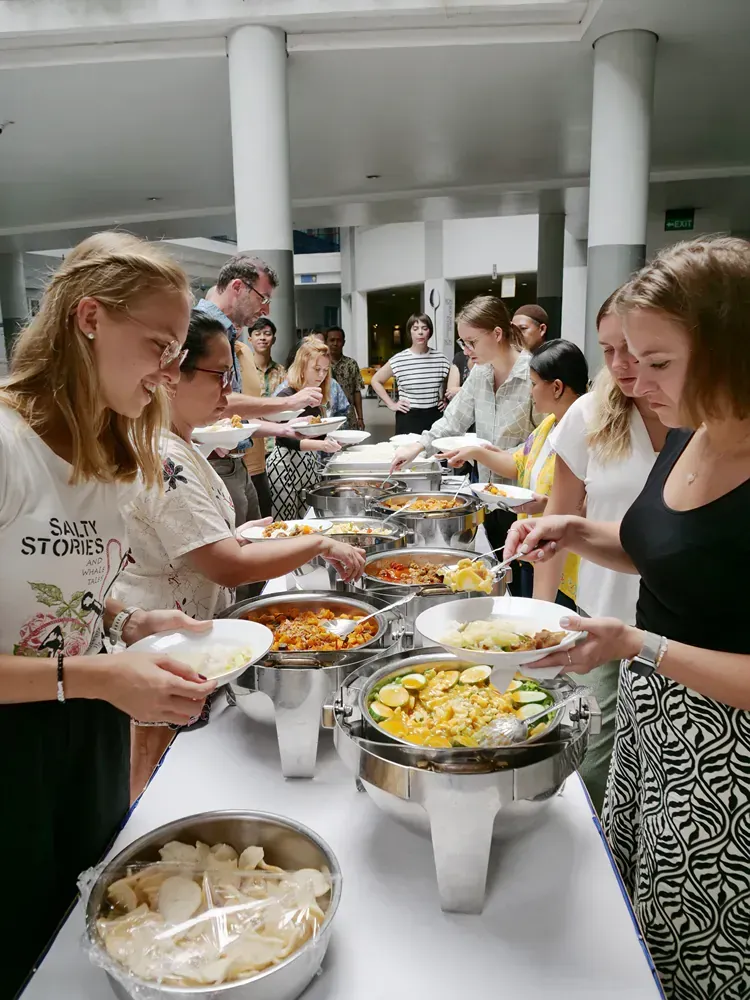 A group of people are standing around a table eating food.