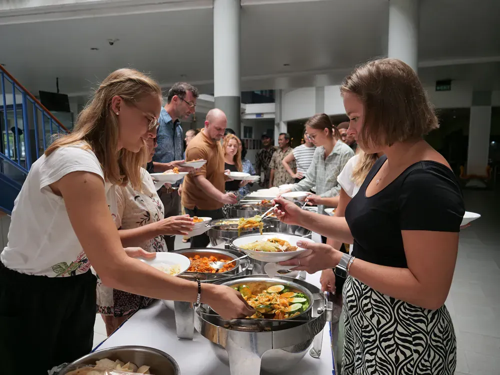 A group of people are standing around a table eating food.