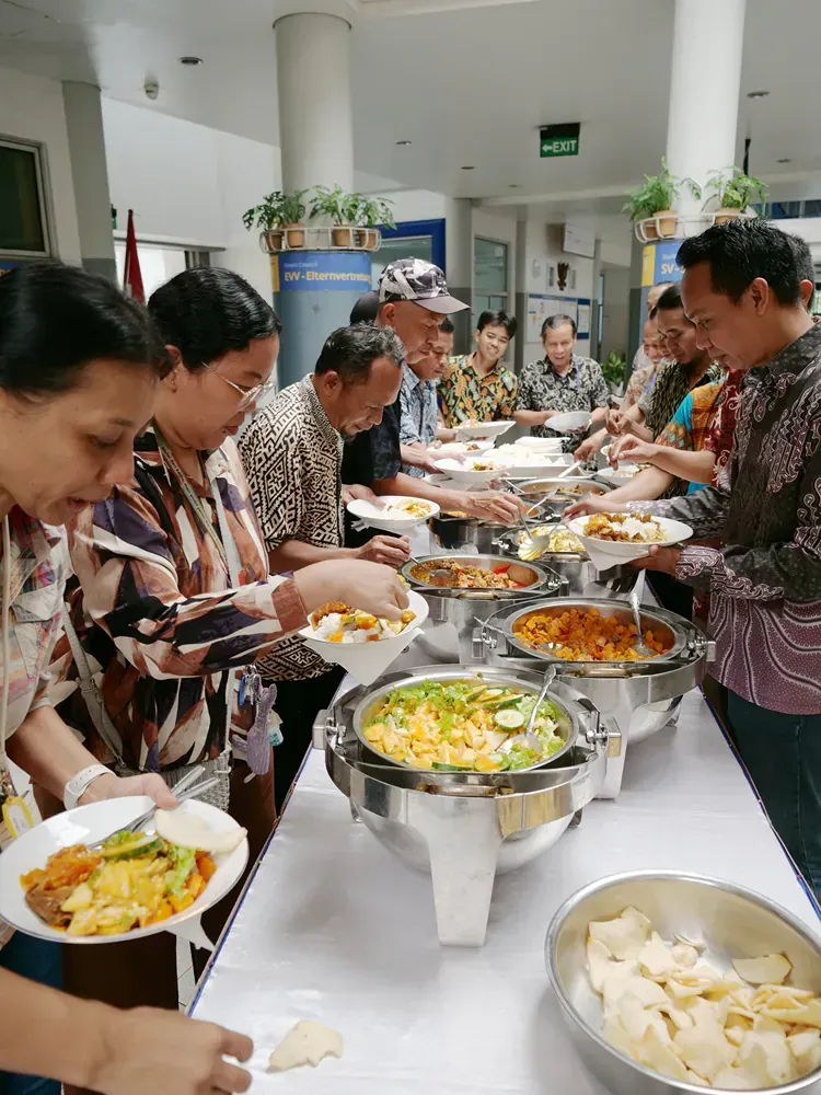A group of people are standing around a buffet table eating food.