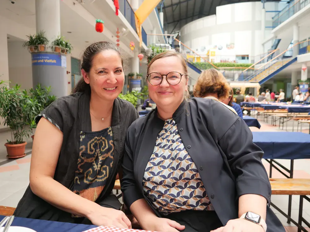 Two women are posing for a picture while sitting at a table.