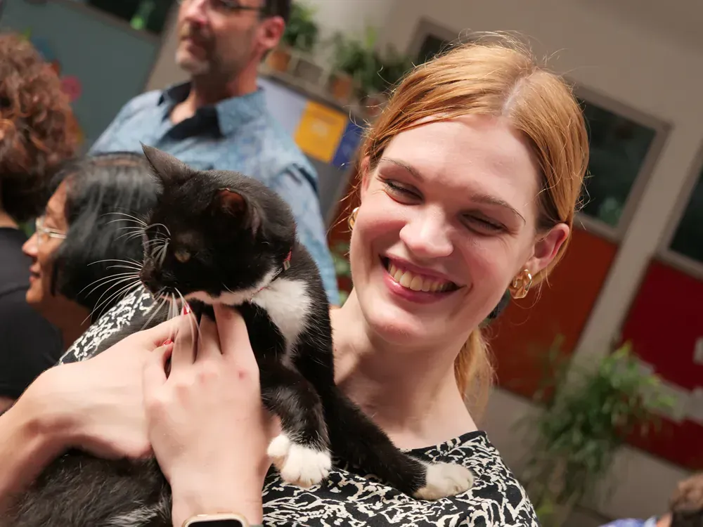 A woman is holding a black and white cat in her arms.