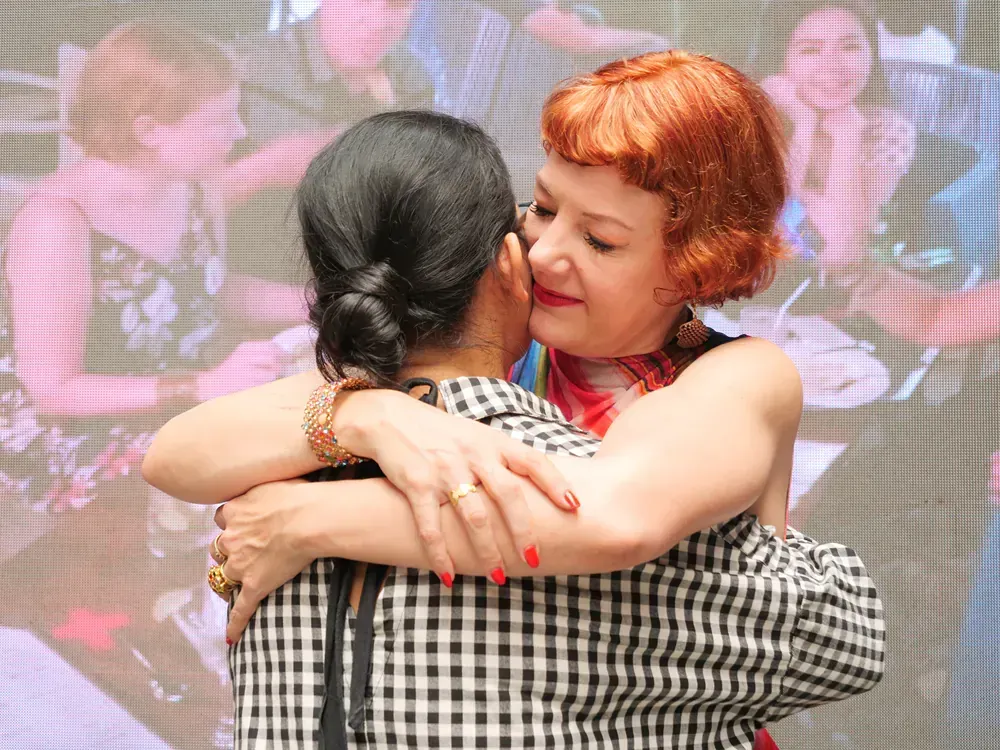 Two women are hugging each other in front of a screen.