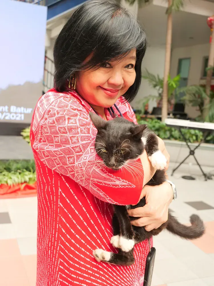 A woman in a red shirt is holding a black and white cat