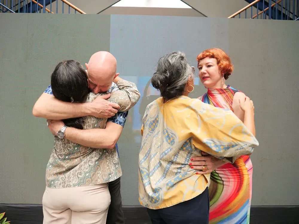 A group of people are hugging each other in front of a projection screen.