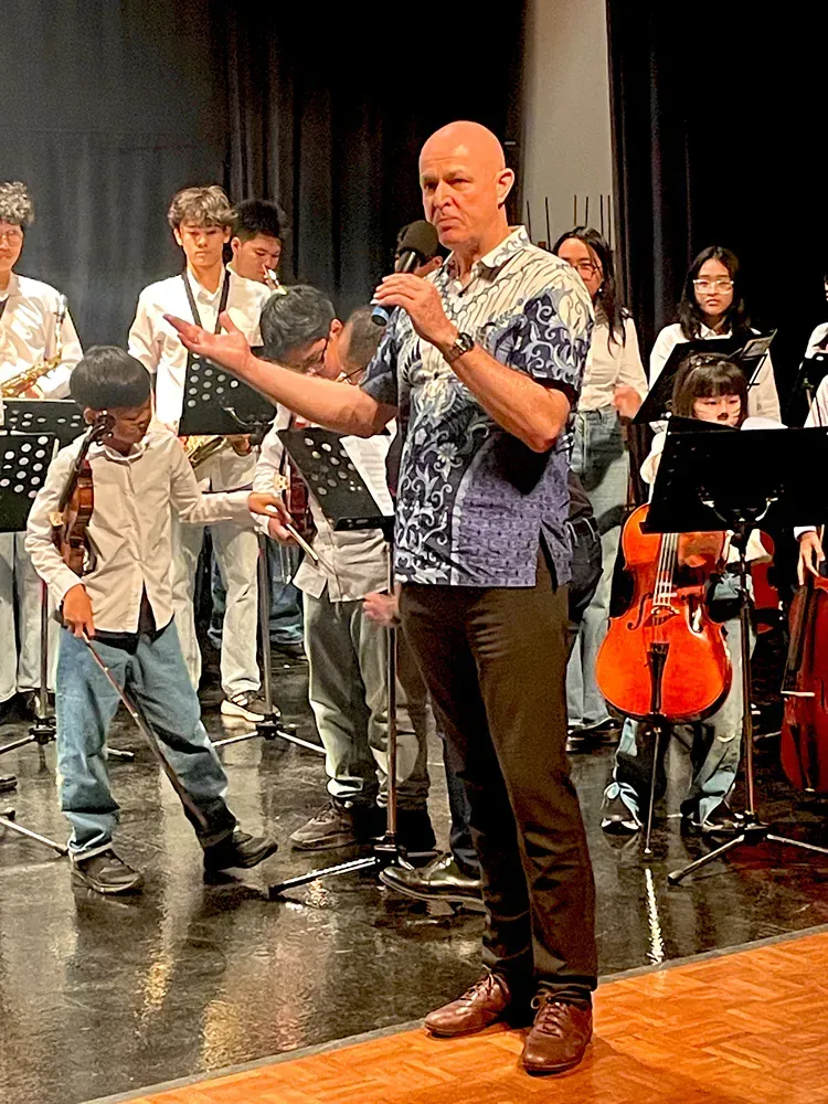 A man is standing on a stage with a microphone in front of an orchestra.