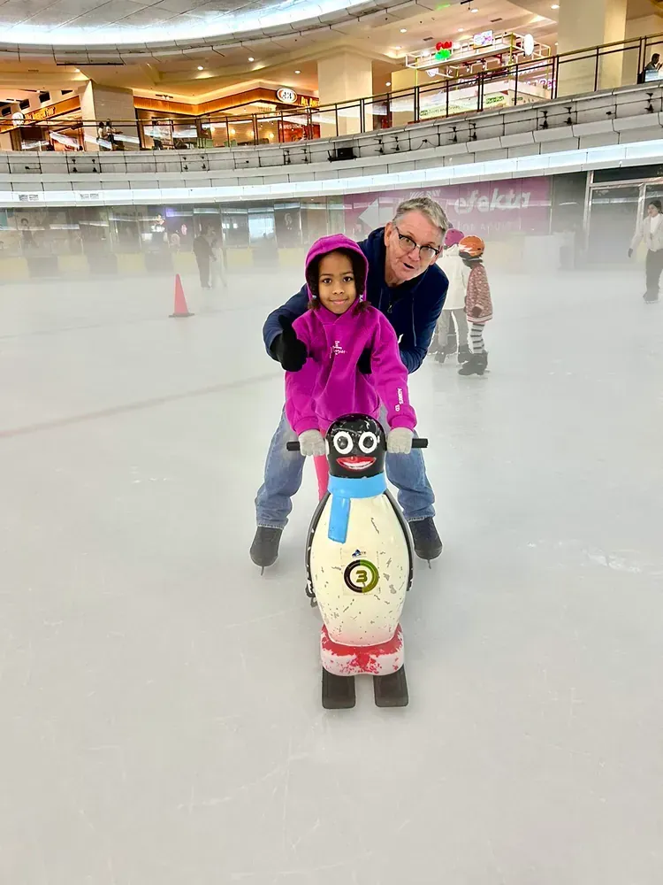 A man and a little girl are riding a penguin on an ice rink.