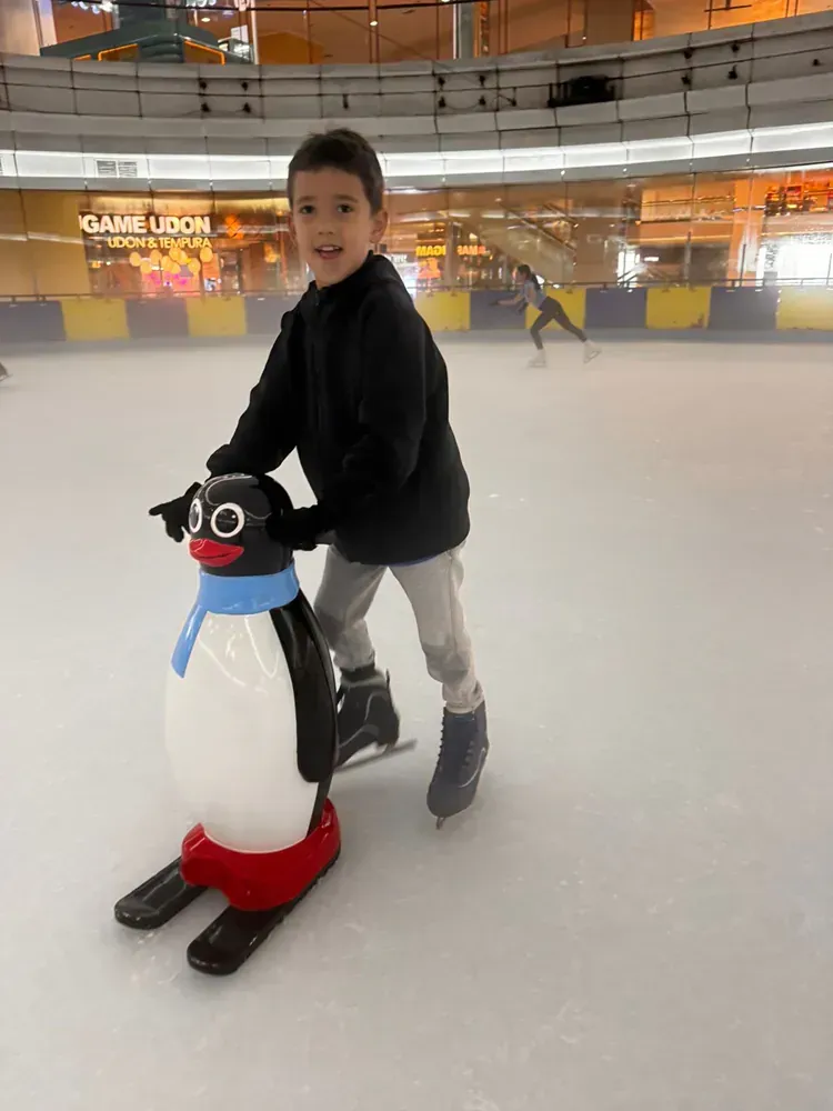 A young boy is riding on the back of a penguin on an ice rink.