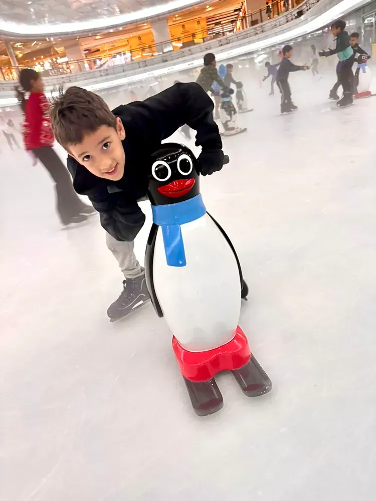 A young boy is standing next to a stuffed penguin on an ice rink.