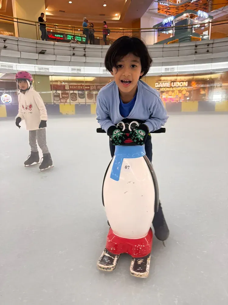 A young boy is riding on the back of a penguin on an ice rink.