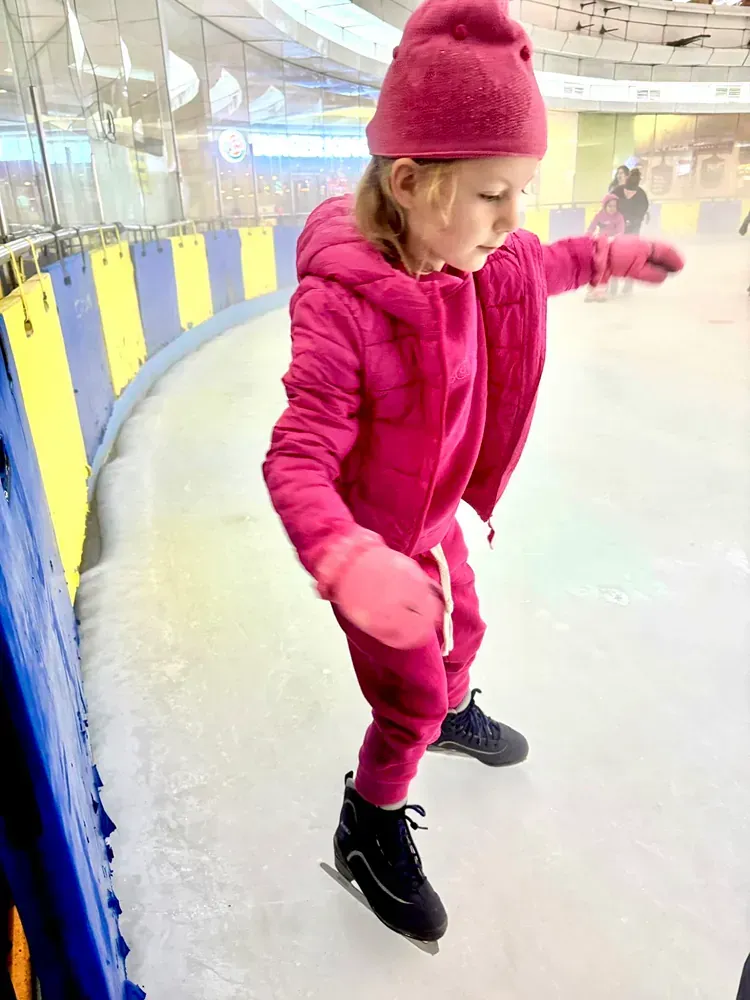 A little girl is ice skating on a rink.