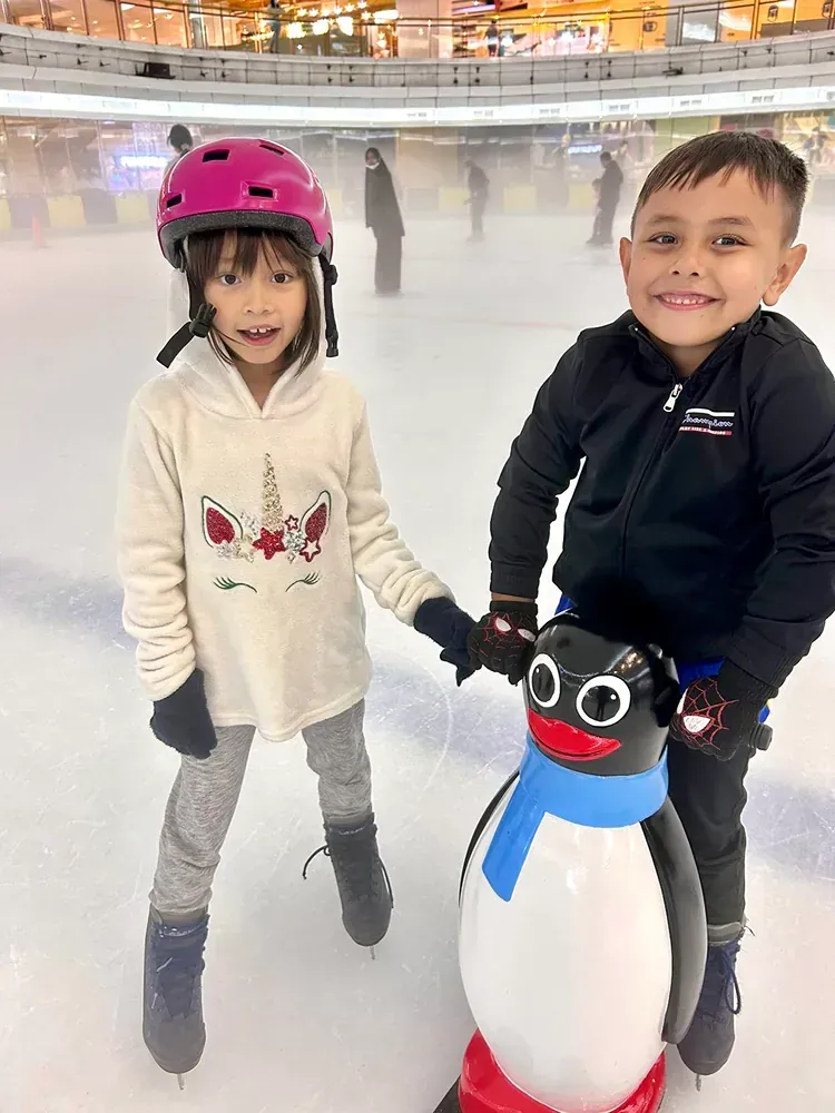 A boy and a girl are standing next to a penguin on an ice rink.