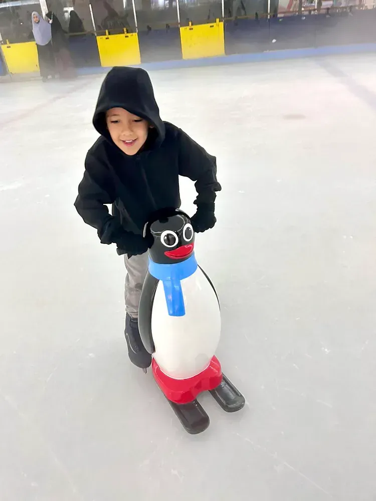 A young boy is riding a penguin on skis on an ice rink