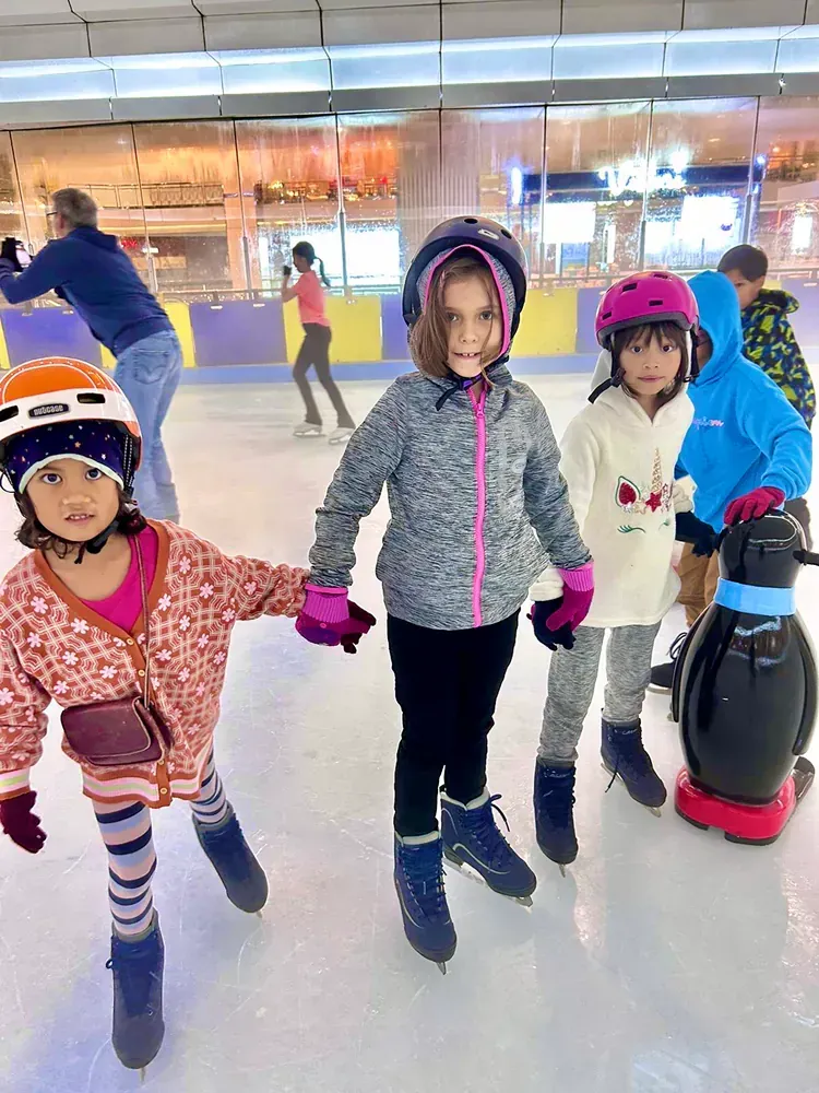 A group of young girls are holding hands while ice skating on a rink.