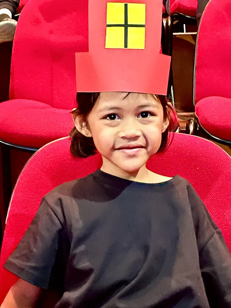 A little girl wearing a red hat with a yellow window on it
