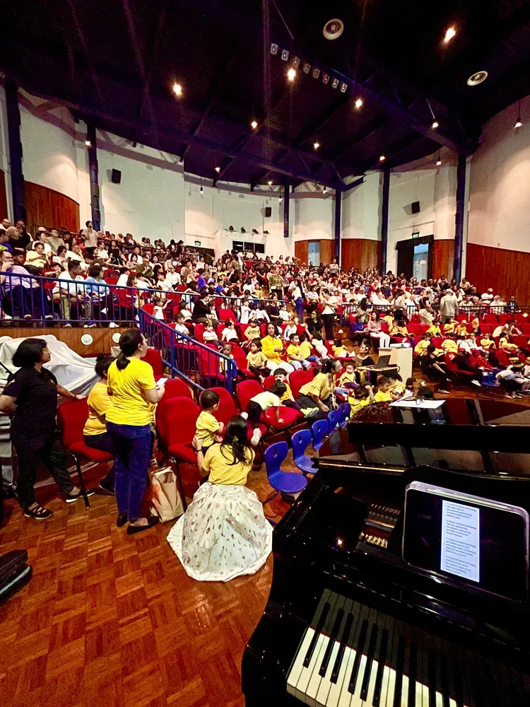 A large auditorium filled with people and a piano in the foreground.