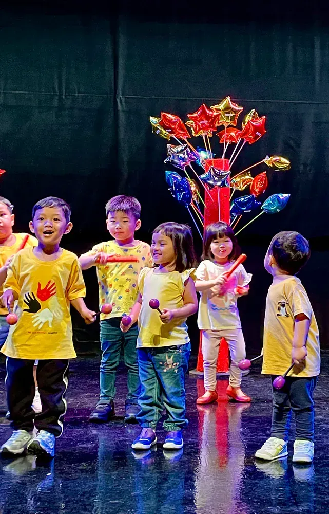 A group of children are standing on a stage holding musical instruments.