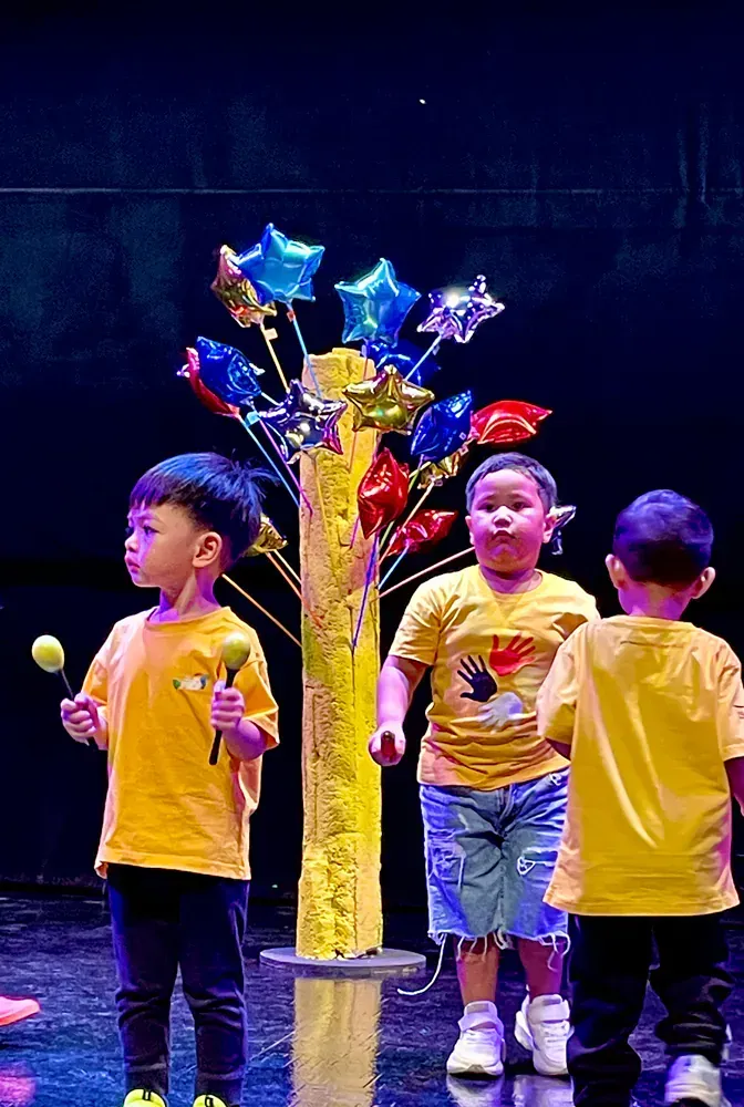 A group of young boys are standing in front of a tree with balloons on it.
