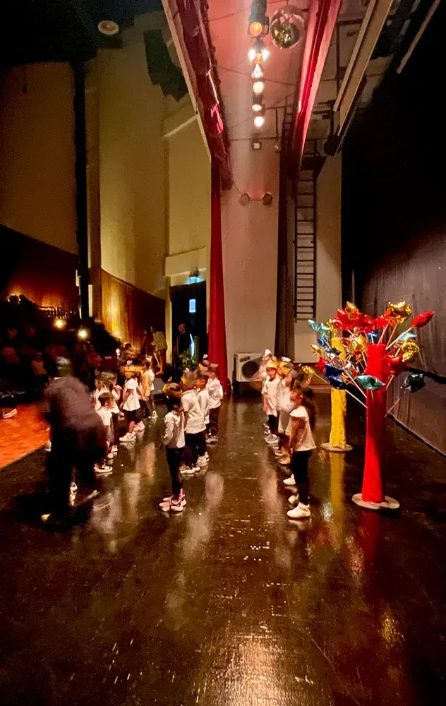 A group of children are standing on a stage in a large auditorium.