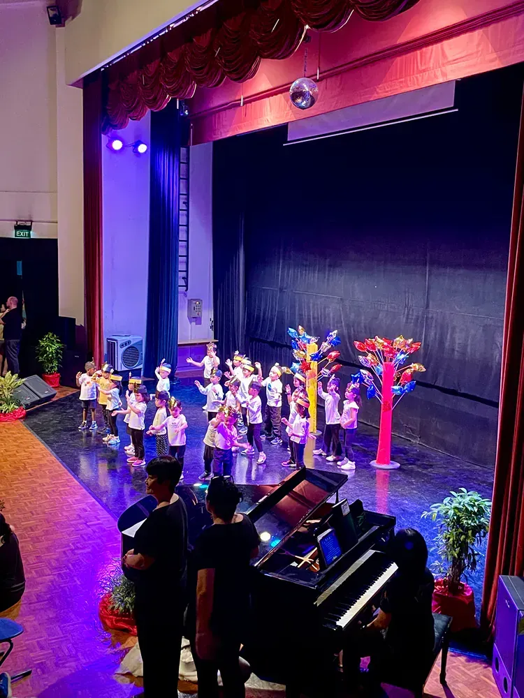 A group of children are standing on a stage in front of a piano.