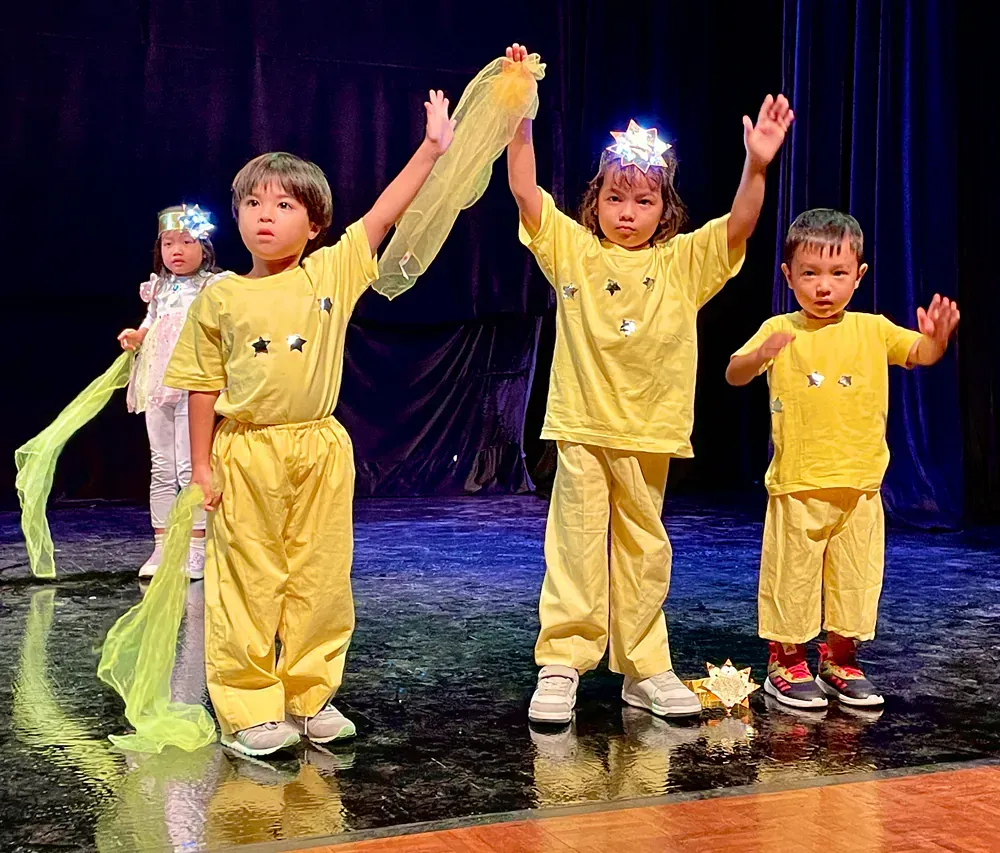 A group of children are standing on a stage with their arms in the air.