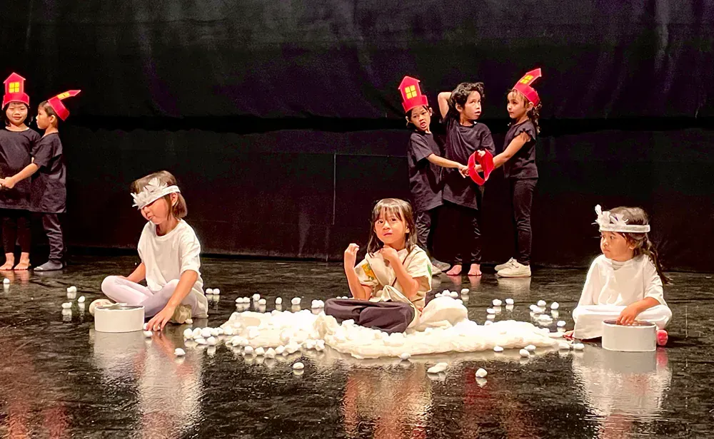 A group of children are sitting on the floor on a stage.