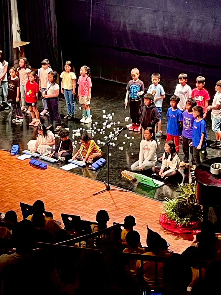 A group of children are singing on a stage in front of a crowd.