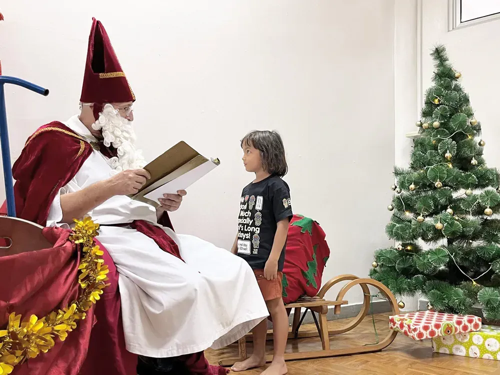 A man dressed as santa claus is reading a book to a young boy in front of a christmas tree.
