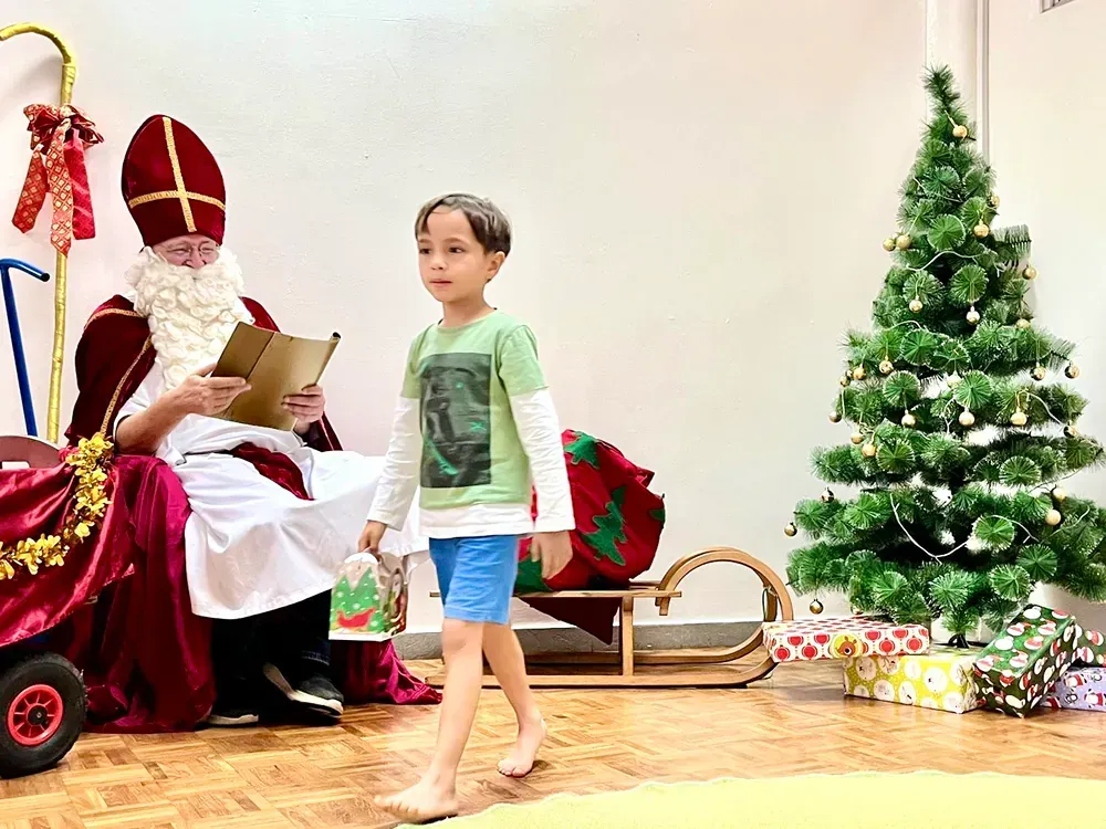 A little boy is walking towards a man dressed as santa claus.