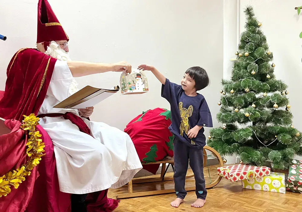 A little boy is giving a gift to santa claus in front of a christmas tree.