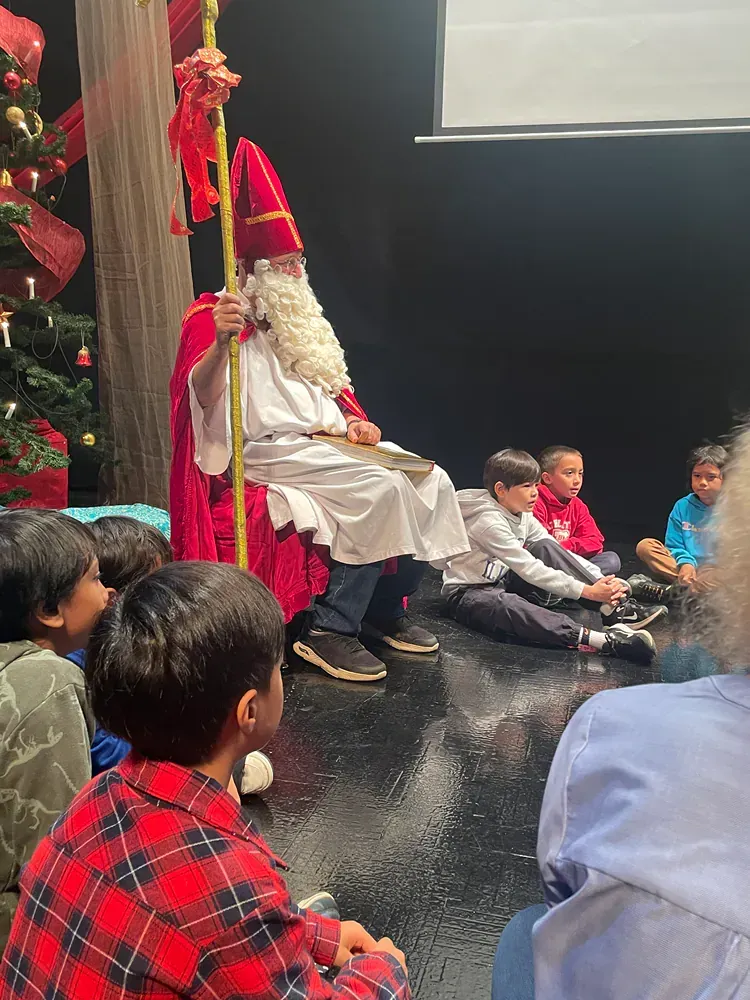 A group of children are sitting on the floor in front of a man dressed as santa claus.