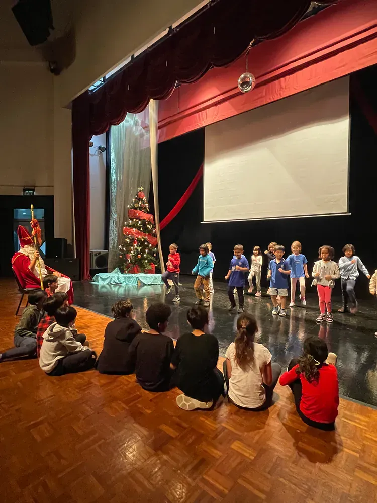 A group of children are sitting on the floor watching a performance on a stage.
