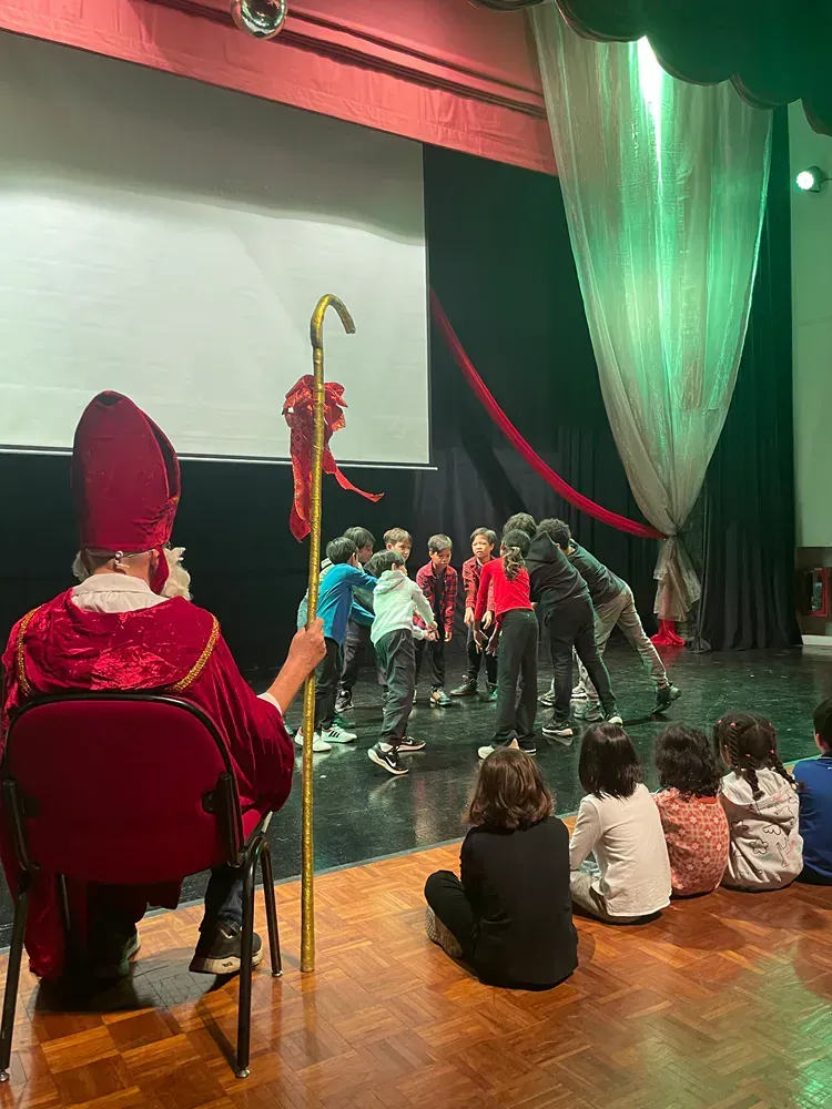 A group of children are sitting on the floor watching a performance on a stage.