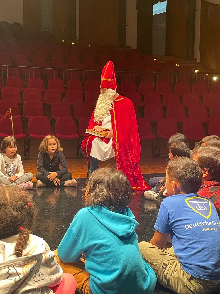 A group of children are sitting on the floor in front of a man dressed as santa claus.