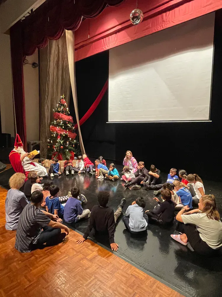 A group of children are sitting on the floor in front of a christmas tree.